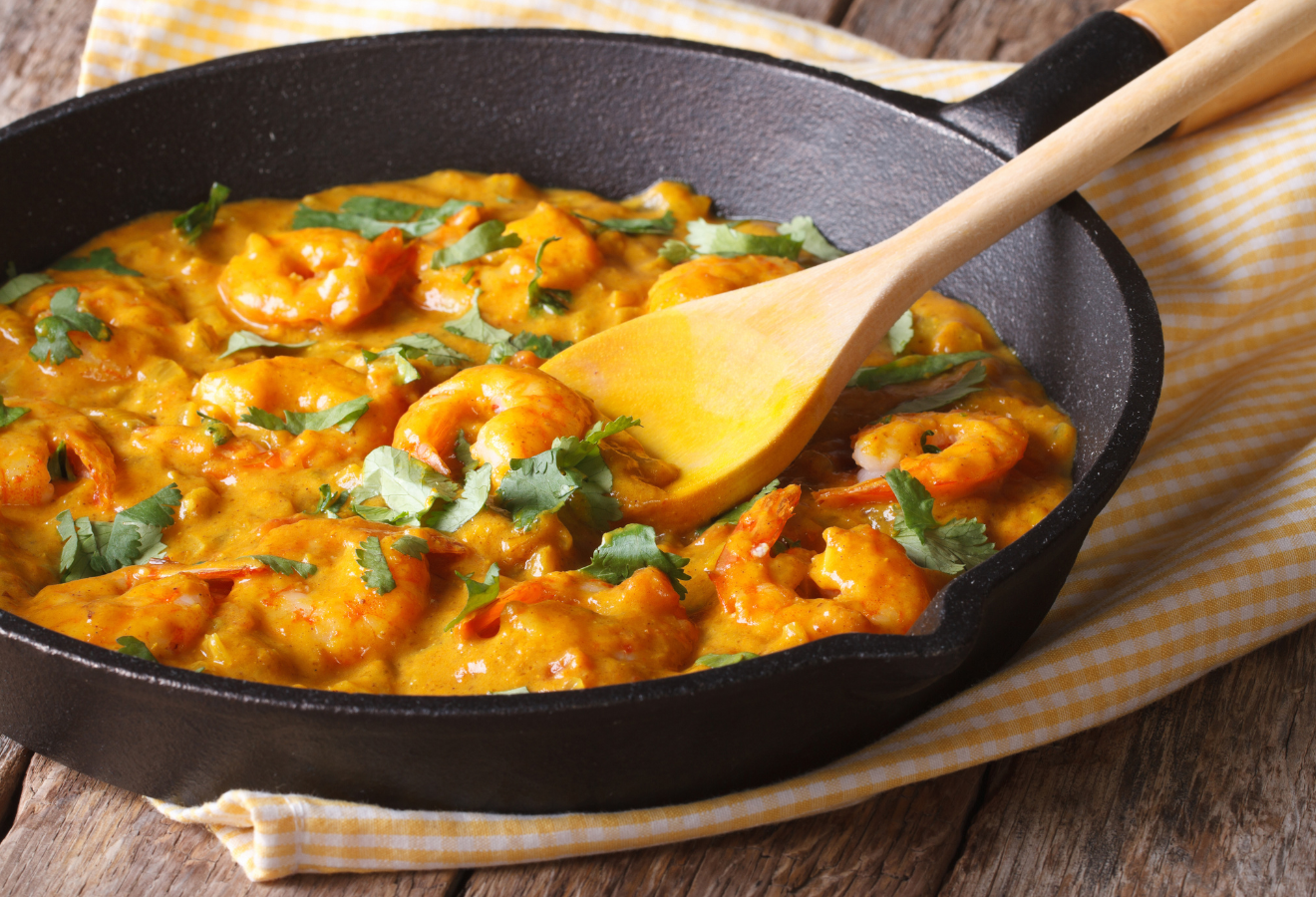 Garnelen-Aprikosen-Curry in einer schwarzen Pfanne im einem Holz-Kochlöffel darin