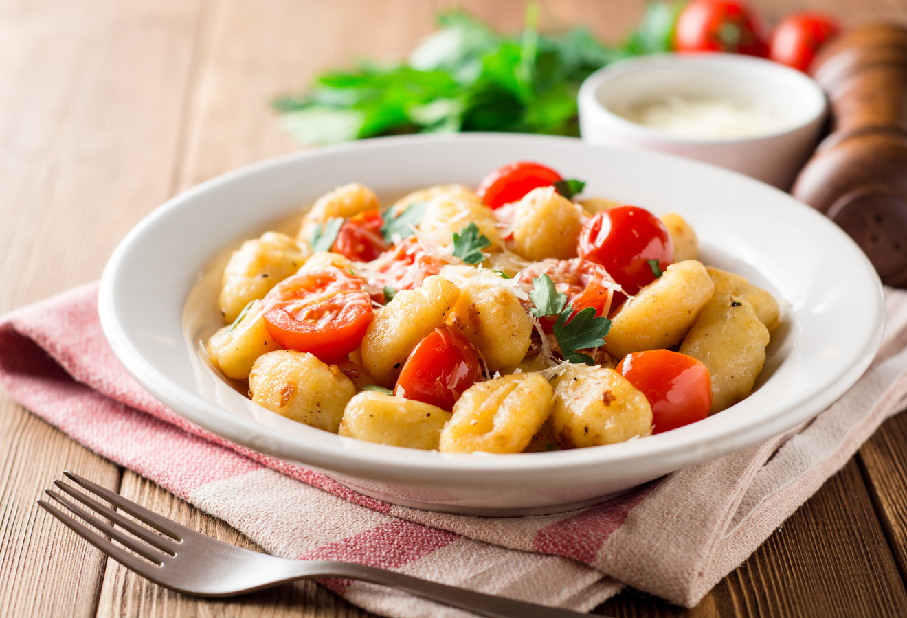  Rosmarin-Gnocchi mit geschmolzenen Tomaten auf einem tiefen Teller, eine Gabel daneben