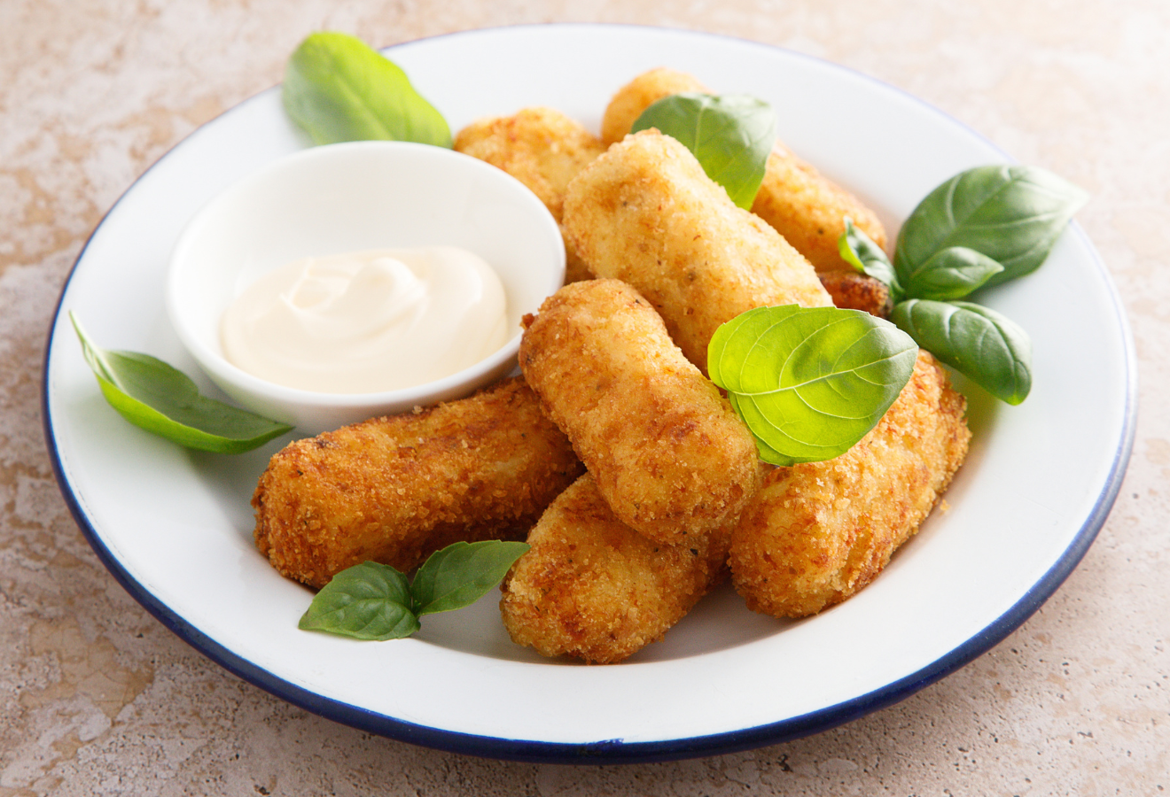 Oliven-Kartoffel-Kroketten auf einem weißen Teller mit Basilikum garniert, daneben ein Schälchen mit Soße