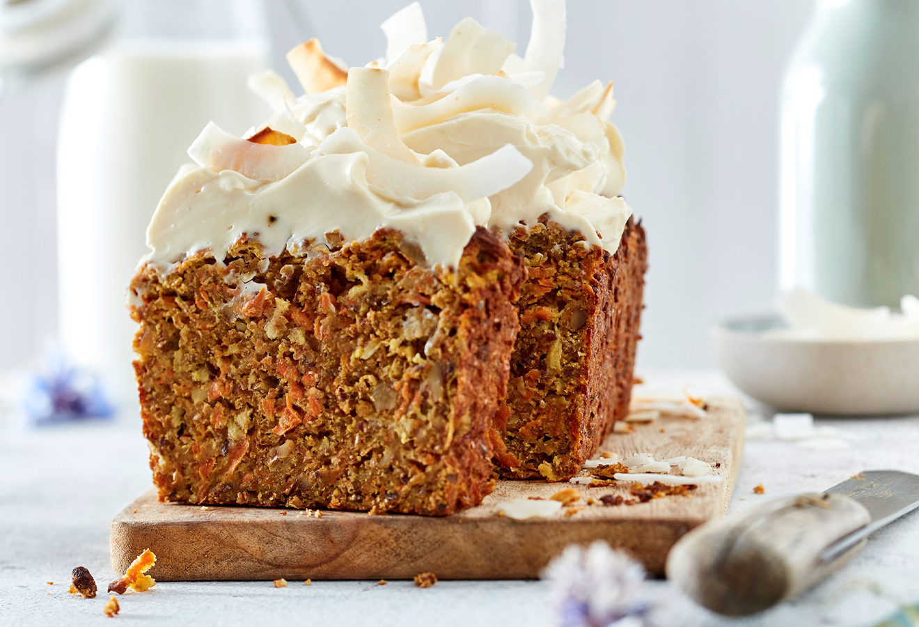 Möhren-Frühstückskuchen mit Kokos-Frischkäse-Frosting auf einem Holzbrett
