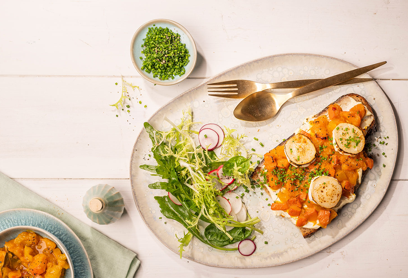 Kürbis-Chutney auf Brot auf einem Teller, daneben Salat und Besteck