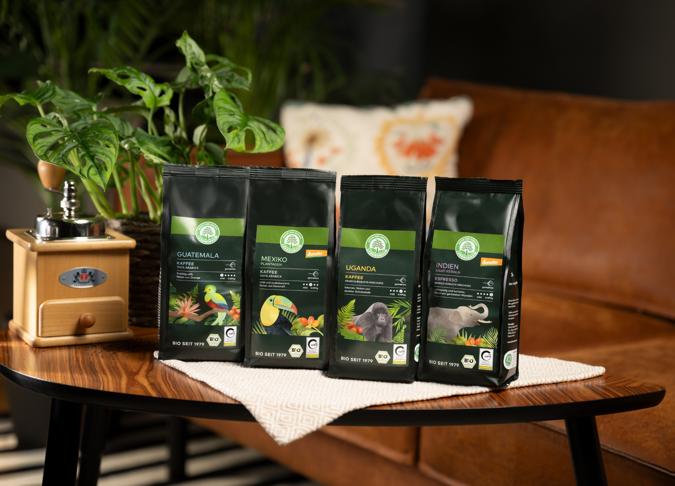 Herkunftskaffeepackungen mit Tiermotiven stehen auf einem Holztisch neben einer Kaffeemühle und einer Pflanze